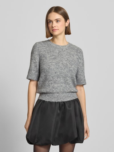 Frauenmodel trägt Strickpullover mit 1/2-Arm und Rundhalsausschnitt von Gina Tricot, Material-Mix mit Lanawoll-Anteil, Regular-Fit, Ziersteinbesatz, graue melierte Textur, kombiniert mit schwarzem Rock, Nahaufnahme Oberkörper.