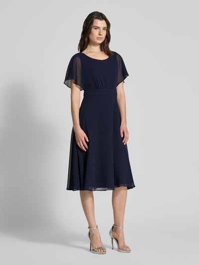 Frauenmodel trägt Knielanges Kleid mit Rundhalsausschnitt von Vera Mont in Dunkelblau, semitransparent, tailliert, blickdichter Unterrock, Ganzkörperansicht von vorne.