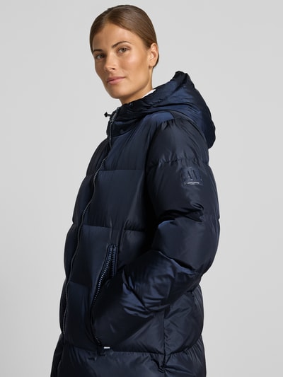 Frauenmodel trägt Steppmantel mit Zweiwege-Reißverschluss von Armani Exchange in dunklem Blau mit Kapuze und Reißverschlusstaschen, Nahaufnahme Oberkörper. Rückenlänge, Passform und Details laut Produktbeschreibung.