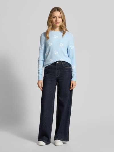 Frauenmodel trägt Regular Fit Strickpullover mit Intarsien Modell 'DOFFY INTARSIA' von Vero Moda in Hellblau mit Allover-Muster, Grobstrick, Rundhalsausschnitt, langen Ärmeln und gerippten Abschlüssen; Ganzkörperansicht von vorne.