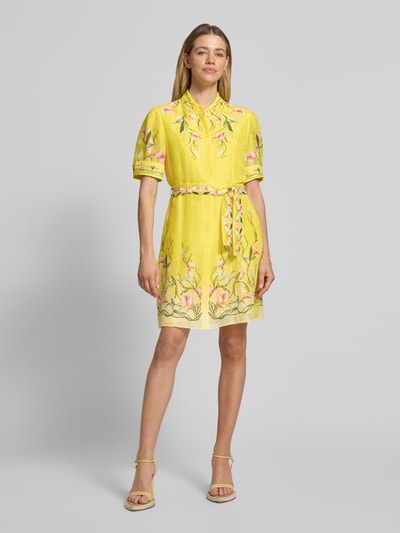 Kobiece modelka nosi Minikleid aus reiner Viskose mit floralem Allover-Print von Marc Cain, żółty kolor, taillowany krój, pasek, krótki rękaw, florystyczny wzór, kołnierzyk, guziki, 93 cm długość tyłu, szerokość w rozmiarze 36: 41 cm, długość rękawa w rozmiarze 36: 29 cm, widok całej sylwetki z przodu.