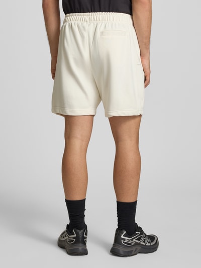 Männermodel trägt Ellesse Shorts mit Logo-Stitching Modell 'ZANICA' in Creme, Baumwoll-Mix, Relaxed Fit, Ganzkörperansicht Rückansicht.