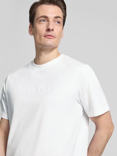 Männermodel trägt T-Shirt mit Rundhalsausschnitt von CK Calvin Klein, Regular-Fit, reine Baumwolle, Logo-Print, Nahaufnahme Oberkörper.