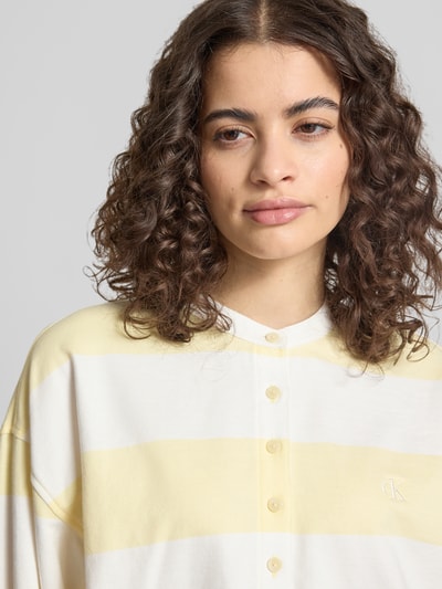 Frauenmodel trägt Relaxed Fit Sweatshirt mit Logo-Stitching Modell 'Varsity' von Calvin Klein Jeans in Weiß mit gelben Streifen, reine Baumwolle, langärmelig, Knopfleiste, Nahaufnahme Oberkörper.