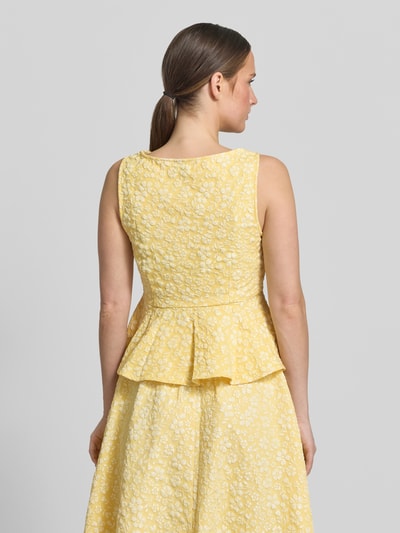 Vrouwenmodel draagt Shaped Fit Schößchen-Top met bloemenpatroon model 'FIONA' van Vero Moda, gele stof met reliëfstructuur, naadritssluiting, peplumdetail, boothals, mouwloos, allover-motief. Volledig beeld van achteren.