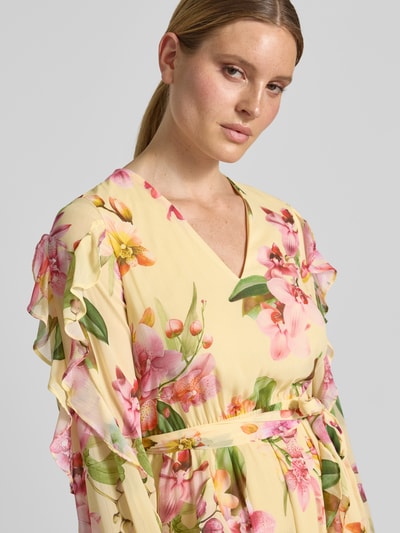 Frauenmodel trägt Knielanges Cocktailkleid mit Chiffons und Bindegürtel von V by Vera Mont in Gelb mit Blumendruck, Volants, Taillierter Schnitt, Allover-Look, V-Ausschnitt, Nahaufnahme Oberkörper.