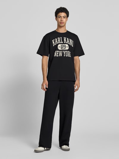 Männermodel trägt Straight Fit Sweatpants mit Gesäßtasche von KARL KANI in Schwarz aus Baumwoll-Mix mit elastischem Bund, Ganzkörperansicht von vorne.