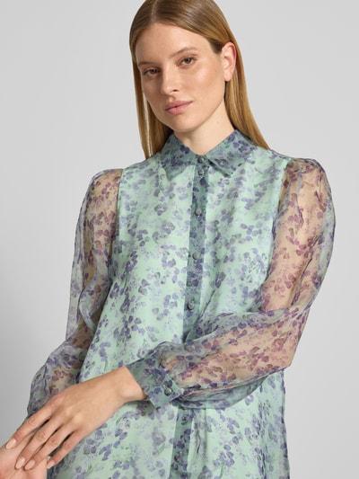Kobiece modelka nosi Knielanges Kleid aus Seide mit Knopfleiste von Marc Cain, kolorowy wzór na całej powierzchni, półprzezroczysty jedwab, prosty krój, kołnierzyk koszulowy, długość do kolan, długość tyłu w rozmiarze 36: 94 cm, szerokość w rozmiarze 36: 50 cm, długość rękawów: 64 cm, z przodu zbliżenie na górną część ciała.