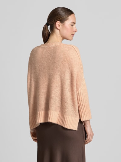 Frauenmodel trägt Oversized Strickjacke mit Alpaka-Anteil von Luisa Cerano in hellem Beige, grobe Struktur, gerippte Abschlüsse, Ganzkörperansicht Rückansicht, Material-Mix, durchgehende Knopfleiste, V-Ausschnitt, Damenmode.