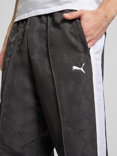 Männermodel trägt Straight Fit Sweatpants mit Logo-Stitching von PUMA PERFORMANCE, Allover-Logo-Print, Ziernähte, Nahaufnahme Oberschenkel.