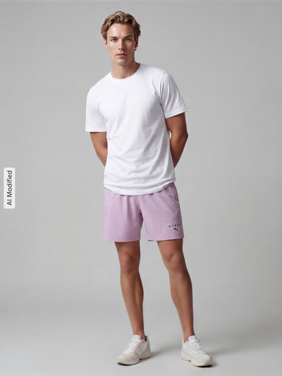 Männermodel trägt Regular Fit Sportshorts mit Label-Print von PUMA Performance in Hellrosa und Weiß auf grauem Hintergrund, Ganzkörperansicht von vorne.