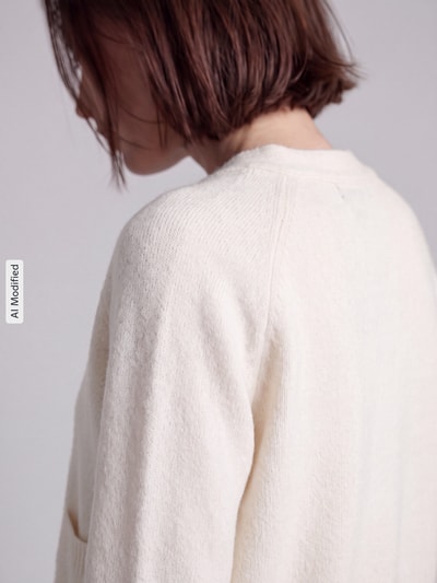 Frauenmodel trägt Oversized Strickjacke mit Woll-Anteil Modell 'BOOM' von VERO MODA in Creme, Struktur fein, Nahaufnahme Oberkörper, KI-modifiziertes Bild.