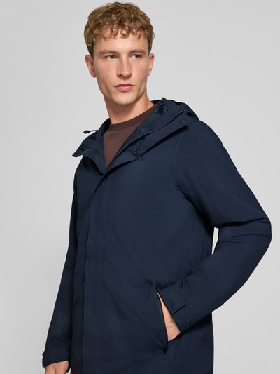 Männermodel trägt Regular Fit Mantel mit Kapuze Modell 'Brussel' von Helly Hansen, dunkelblau, glatte Textur, Nahaufnahme Oberkörper. Rückenlänge 96 cm, Schulterbreite 46 cm, Brustweite 51 cm, Ärmellänge 66 cm.