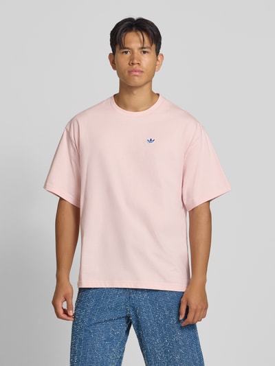 Männermodel trägt Relaxed Fit T-Shirt aus reiner Baumwolle Modell 'SUMMER GRAPHIC' von adidas Originals in Hellrosa, Ganzkörperansicht von vorne.