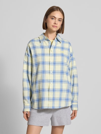 Frauenmodel trägt Relaxed Fit Hemdbluse aus reiner Baumwolle Modell 'Vivian' von OH APRIL, kariert in Blau und Gelb, Logo-Patch, Ganzkörperansicht von vorne.