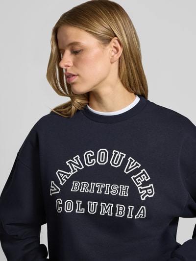 Frauenmodel trägt dunkelblaues Sweatshirt aus Baumwoll-Mix Modell 'MERLE' von JIXX mit weißem Statement-Print, Nahaufnahme Oberkörper.
