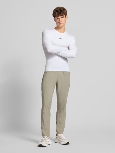 Männermodel trägt Longsleeve mit Label-Print von adidas Training in Weiß, Slim Fit, Material-Mix mit Stretch, Ganzkörperansicht von vorne.