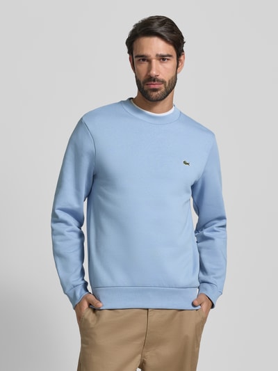 Męski model nosi Classic Fit Sweatshirt aus Baumwoll-Mix od Lacoste, jednokolorowa, wyhaftowane logo, okrągły dekolt, mieszanka bawełny, efekt: smooth, krój: klasyka, długi rękaw, prążkowane zakończenia. Ganzkörperansicht von vorne.