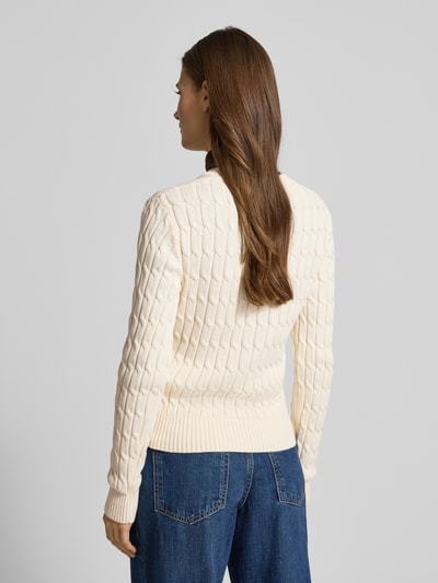 Frauenmodel trägt Slim Fit Strickpullover aus reiner Baumwolle von Tommy Hilfiger in Zopfmuster, Strickoptik, cremefarben, Ganzkörperansicht Rückansicht.