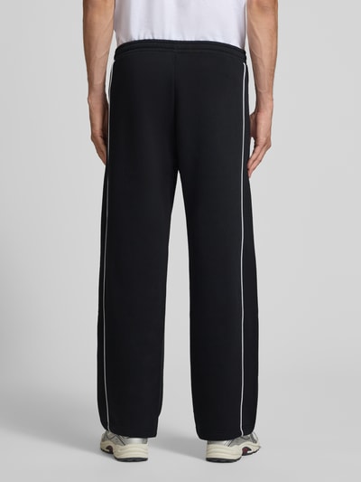 Männermodel trägt Straight Fit Sweatpants aus reiner Baumwolle mit Label-Patch von REVIEW, schwarze Farbe, Ganzkörperansicht Rückansicht. Innenbeinlänge bei Größe M 40 cm, elastischer Bund, seitliche Eingrifftaschen, glatte Textur.