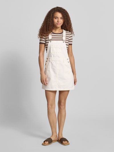 Frauenmodel trägt Leicht ausgestelltes Jeanskleid aus reiner Baumwolle von Tommy Jeans in Denim-Optik, Label-Stitching-Applikation, Mini-Länge, Karree-Ausschnitt, Latzträger, Brusttasche, seitliche Eingrifftaschen, Optik: Denim, Passform: Leicht Ausgestellt, Material: Reine Baumwolle, Ganzkörperansicht von vorne.