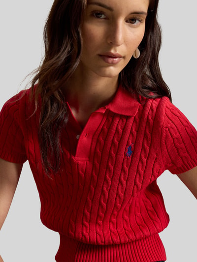 Frauenmodel trägt Regular Fit Strick-Poloshirt aus reiner Baumwolle von Polo Ralph Lauren in Rot mit Zopfmuster, Nahaufnahme Oberkörper.