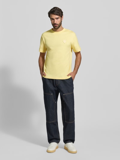 Męski model nosi Regular Fit T-Shirt aus reiner Baumwolle Modell 'JERSEY LOURD' od Lacoste, jednolity żółty, krótki rękaw, całkowity widok z przodu.