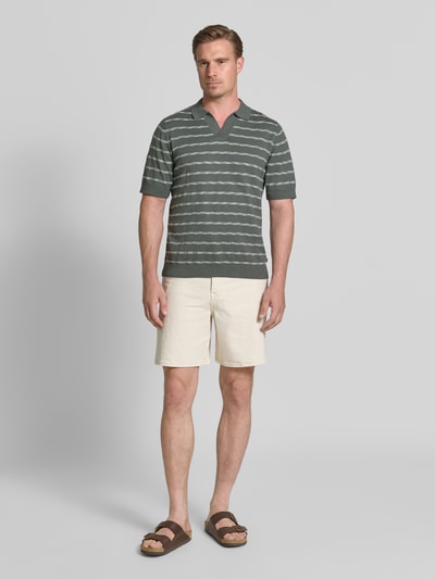 Männermodel trägt Regular Fit Poloshirt aus reiner Baumwolle von Tom Tailor in Dunkelgrün mit weißen Streifen, Ganzkörperansicht von vorne.