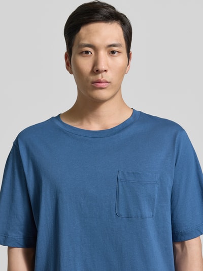 Męskimodel nosi T-Shirt mit Rundhalsausschnitt und Brusttasche von Schiesser, mieszanka bawełny i lnu, krój regular fit, okrągły dekolt, brustasza, długość tyłu w rozmiarze 50: 70 cm, niebieski odcień, gładka faktura, z przodu detal kieszeni, jasne tło, półzbliżenie przód