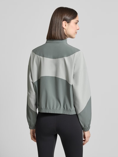 Frauenmodel trägt Trainingsjacke mit Stehkragen und Eingrifftaschen von Under Armour in Grau, Regular-Fit, Rückenlänge 60 cm, Schulterbreite 62 cm, Brustweite 57 cm, Ärmellänge 50 cm, Ganzkörperansicht Rückansicht.