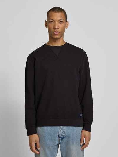 Männermodel trägt Regular Fit Sweatshirt mit Rundhalsausschnitt van Scotch & Soda in zwart katoenmix met labeldetail, heren, ganzkörperansicht van voren. Ruglengte maat M 68 cm, mouwlengte maat M 65 cm.