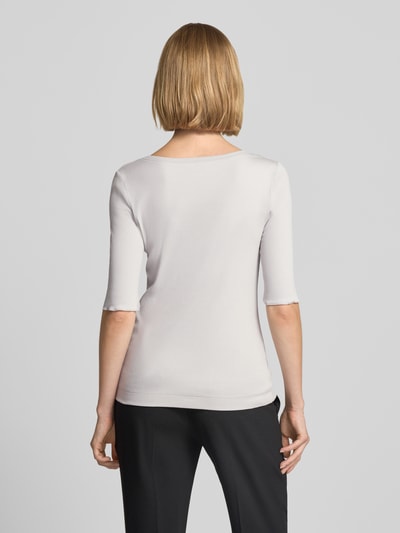 Frauenmodel trägt T-Shirt mit Rundhalsausschnitt und Label-Detail von Marc Cain, Baumwoll-Elasthan-Mix, schlichte helle Farbe, Rückenlänge 55 cm, Ganzkörperansicht Rückansicht.