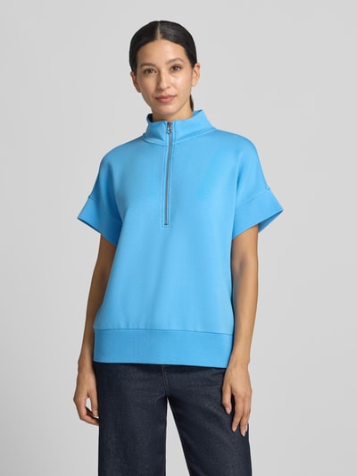 Frauenmodel trägt Sweatshirt mit Troyer-Kragen Modell 'Ritchie' von VARLEY in leuchtendem Blau, lockerer Schnitt, Kurzarm, elastischer Viskose-Mix, Ganzkörperansicht von vorne.