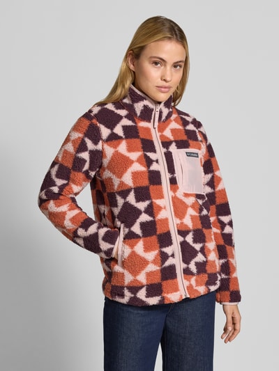 Modelka nosi Regular Fit Jacke mit Stehkragen od Columbia, polar z geometrycznym wzorem, z kieszeniami napoleonową i wpuszczanymi, zamek, długość tyłu w rozmiarze S: 61 cm, szerokość ramion w rozmiarze S: 39 cm, szerokość w biuście w rozmiarze S: 49 cm, długość rękawa w rozmiarze S: 63 cm, kolory różowy, fioletowy, pomarańczowy, krój regular fit, widok całej sylwetki z przodu.