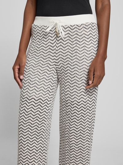 Vrouwenmodel draagt Schlupfhose im Allover-Look mit Tunnelzug van comma in regular fit, elastische band, zwart-wit zigzag patroon, all-over look, dames, context: elastische band, tunnelkoord, bandwijdte maat 36: 38 cm, binnenbeenlengte maat 36: 73 cm, nahaufnahme bovenlichaam.