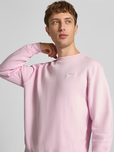 Männermodel trägt Relaxed Fit Sweatshirt aus Baumwoll-Mix von Nike in zartem Rosa mit glatter Textur, Nahaufnahme Oberkörper. Herren Sweatshirt.
