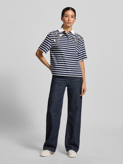 Frauenmodel trägt T-Shirt mit Polokragen von Rich & Royal, reine Baumwolle, Regular Fit, kurze Knopfleiste, Zierbesatz, navy-weiß gestreift, kombiniert mit dunkelblauen Jeans, Ganzkörperansicht von vorne.