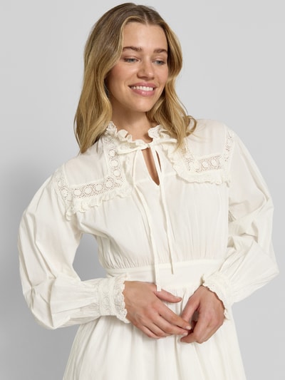 Frauenmodel trägt knielanges Kleid mit Rüschenbesatz Modell 'Gilara' von mbyM in Creme, Reine Baumwolle, Taillierte Passform, Langärmelig, Stehkragen, Schlüssellochausschnitt, eingefasste Ärmelabschlüsse, Nahaufnahme Oberkörper.
