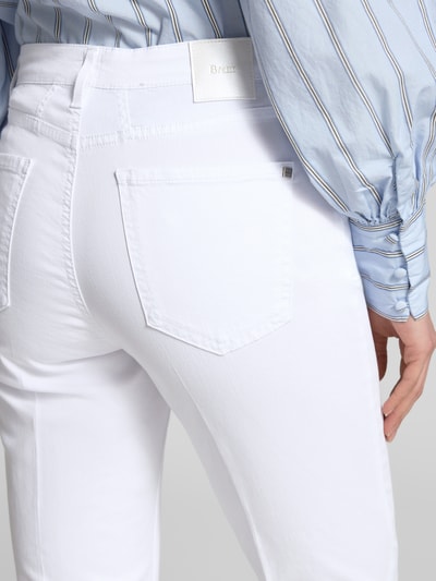 Männermodel trägt białe Bootcut Jeans im 5-Pocket-Design Modell 'Mary' von Brax z mieszanki bawełny i lyocellu z dodatkiem streczu, detal z logo, szerokość w rozmiarze 36: 39 cm, długość wewnętrzna nogawki 67 cm, detailaufnahme.