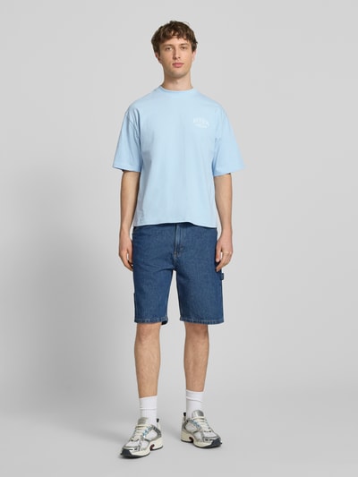 Männermodel trägt T-Shirt mit Label-Detail von REVIEW in Hellblau, Reine Baumwolle, Lockerer-Schnitt, Rundhalsausschnitt, 1/2-Arm, Rückenlänge 68 cm bei Größe M, Ganzkörperansicht von vorne.