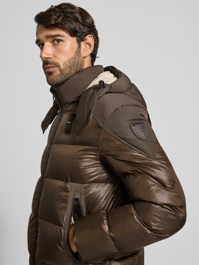 Männermodel trägt Steppjacke mit Zweiwege-Reißverschluss Modell 'KIERNAN' von Blauer USA in Braun, glatte Oberfläche, Regular Fit, Nahaufnahme Oberkörper, kontekst: męska kurtka puchowa z kapturem, detal z logo, długość tyłu w rozmiarze M: 67 cm, szerokość w ramionach: 49 cm, szerokość w rozmiarze M: 59 cm, długość rękawa: 65 cm.