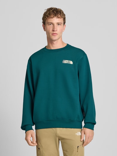 Männermodel trägt Relaxed Fit Sweatshirt aus Baumwoll-Mix von The North Face in Dunkelgrün mit Logo-Print, Ganzkörperansicht von vorne.