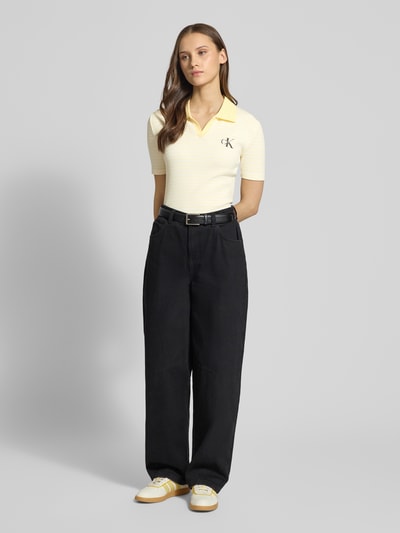 Frauenmodel trägt Slim Fit Poloshirt mit Label-Stitching von Calvin Klein Jeans in Ripp-Optik, V-Ausschnitt, Ganzkörperansicht von vorne.