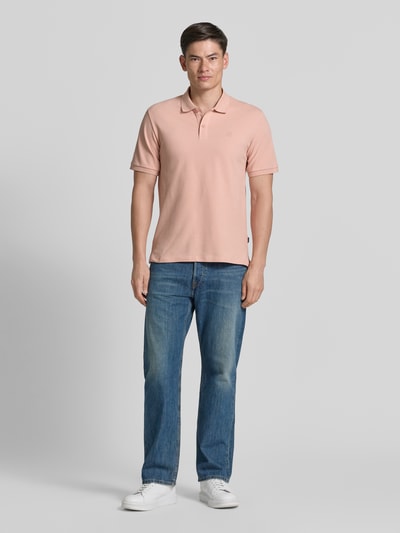 Männermodel trägt Slim Fit Poloshirt mit Stitching von Jack & Jones Premium in Hellrosa, reine Baumwolle, Knopfleiste, Ganzkörperansicht von vorne.