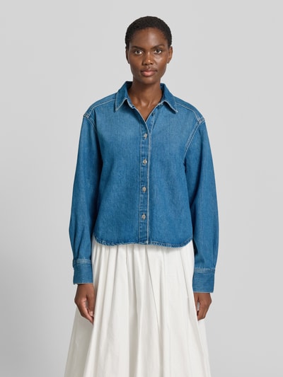 Frauenmodel trägt Relaxed Fit Jeansbluse mit Knopfleiste Modell 'CELIA' von Samsøe Samsøe aus reiner Baumwolle, Hemdblusenkragen, mittelblau, Ganzkörperansicht von vorne.