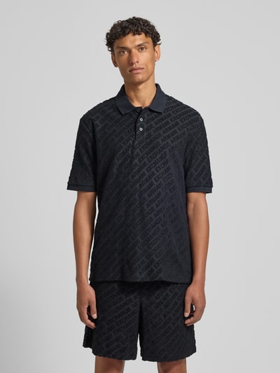 Männermodel trägt Slim Fit Poloshirt mit Logo-Muster von ARMANI EXCHANGE in Dunkelblau, Baumwoll-Mix, Knopfleiste, Ganzkörperansicht von vorne.