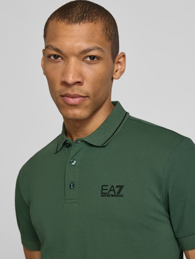 Męski model nosi Regular Fit Poloshirt mit Logo-Print od EA7 Emporio Armani, bawełna elastyczna, zielony, logo, polo, krótki rękaw, zbliżenie na górną część ciała