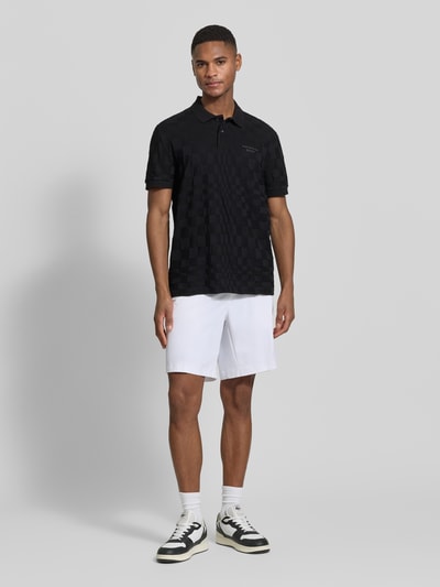 Männermodel trägt Relaxed Fit Bermudas mit Label-Schriftzug Modell 'SPIRIT70' von BOSS Green X PORSCHE, unifarben in Weiß, Ganzkörperansicht von vorne.