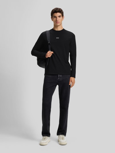 Męski model nosi Regular Fit Langarmshirt aus Baumwoll-Mix Modell 'TCHARK' von BOSS Orange, czarny, gładki, długi rękaw, dekolt okrągły, z nadrukiem-logo, krój regular fit, widok całej sylwetki z przodu.