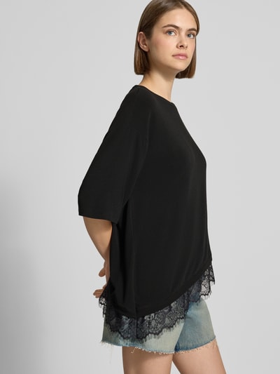 Frauenmodel trägt schwarzes Modell 'GLAMOUR' T-Shirt von ONLY mit Spitzenbesatz zu Jeansshorts, Ganzkörperansicht von vorne. Damen T-Shirt von ONLY.